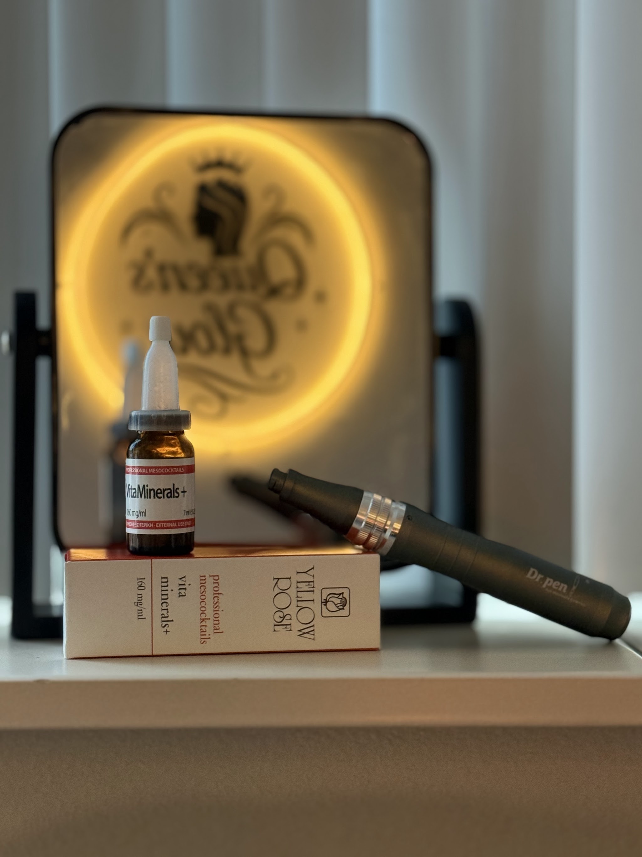Het verlichte Queen’s Glow-bord achter een flesje Yellow Rose en een microneedling pen